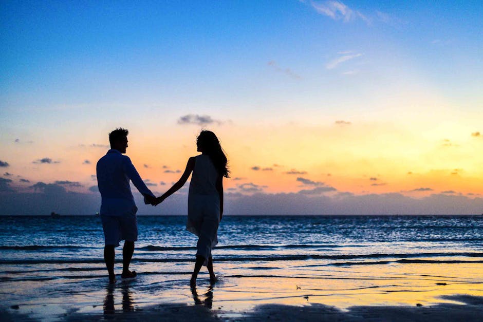 A romantic couple walks hand in hand on a tropical beach at sunset
